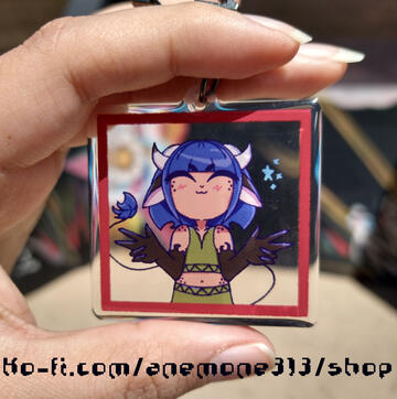 image of an acrylic keychain of my original character, halcyon, doing double peace signs. the acrylic is clear so you can see the background behind the character